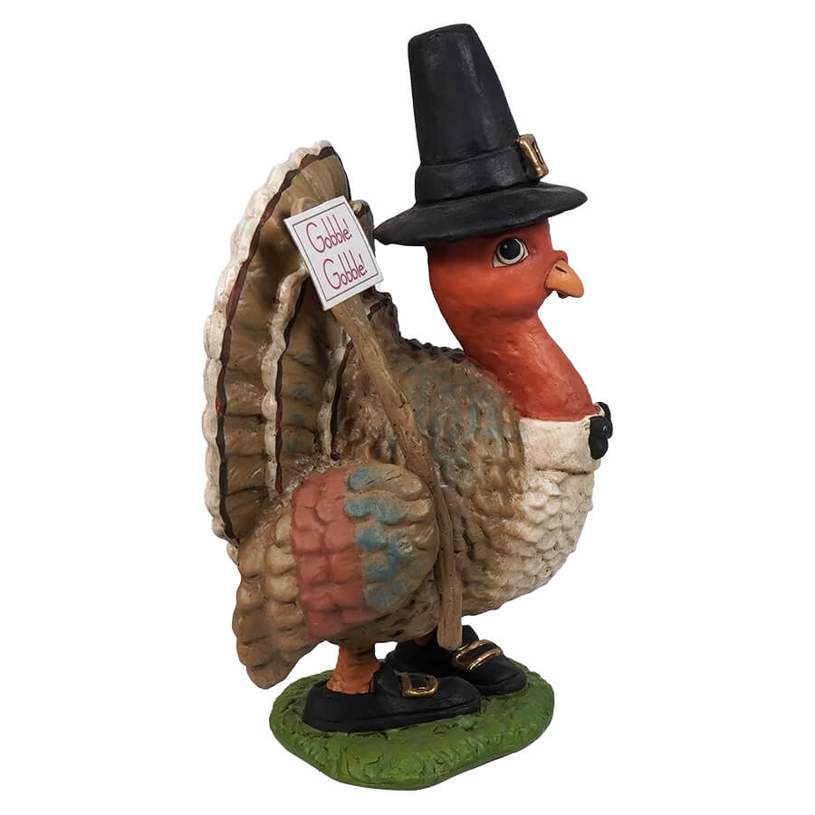 Decorative turkey figurine wearing a pilgrim hat and holding a ’Don’t Shoot!’ sign.