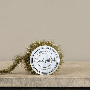 A spool of shimmering gold tinsel garland with a white label reading ragon house 6 tinsel garland bolivar ohio holiday garlands
