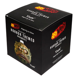 Black box showing gorenaments chum halloween ornament with greenish golden textured mask and orange eyes pumpkin ornament