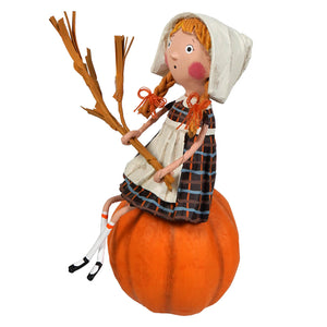A lori mitchell grateful greta figurine with orange braided hair sitting on a pumpkin holding a rustic broom thanksgiving decor
