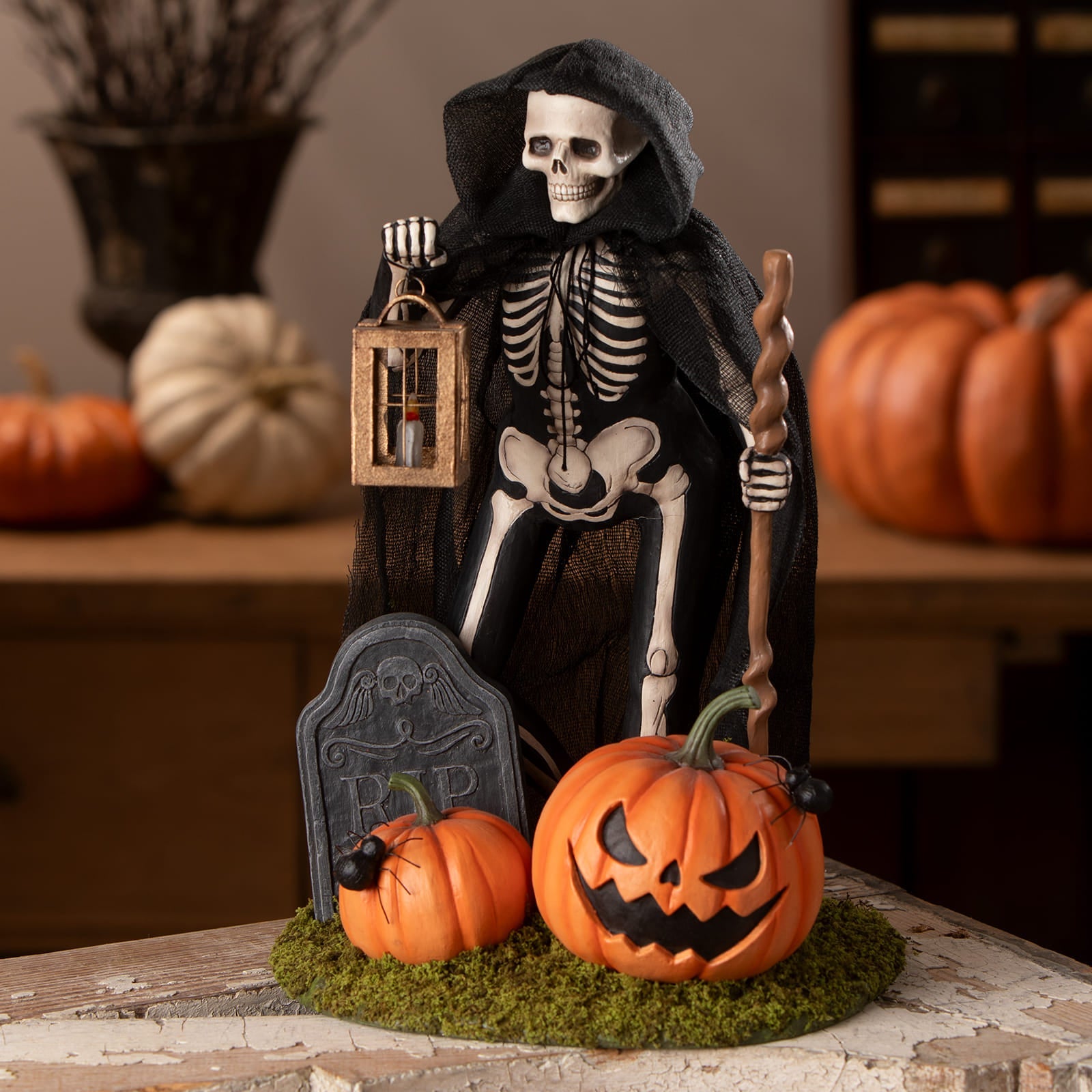 Graveyard gideon skeleton decor figure in black and white holding lantern and staff beside carved pumpkins on mossy base
