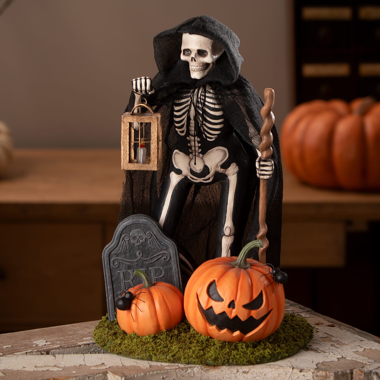Black-cloaked graveyard gideon skeleton figurine holding lantern and staff with carved pumpkins on mossy base for skeleton decor figures and ornaments