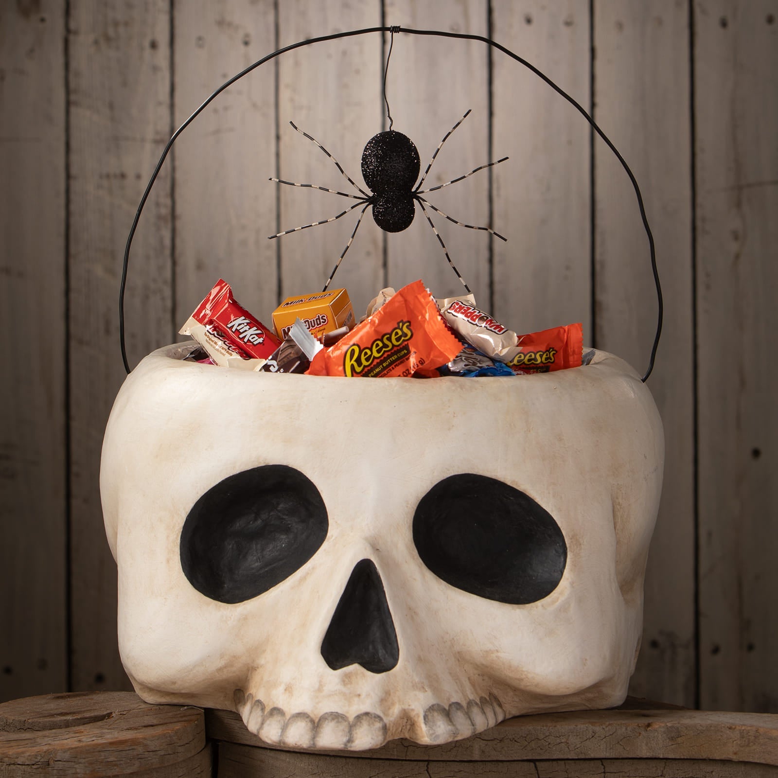 A white skull-shaped grim bucket halloween bucket with black eye sockets and a spider on the wire handle