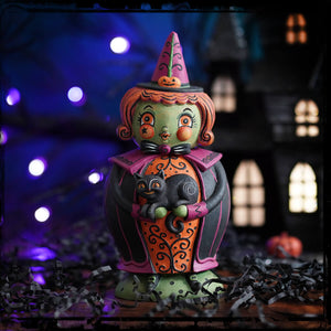 A whimsical green witch figurine with orange hair and pink hat holding a black cat in the jack spooks jar with jack o lantern detail