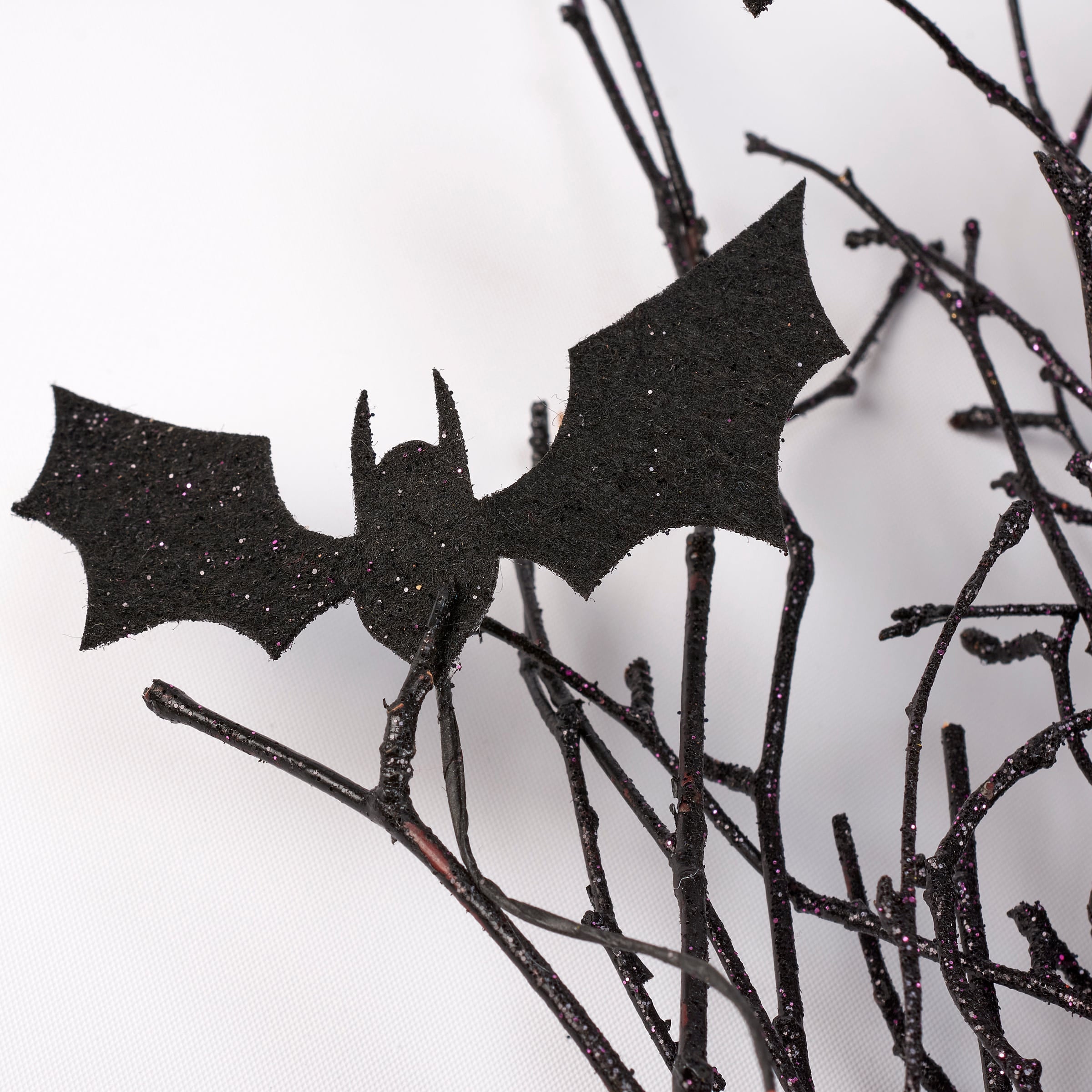 Black glittery halloween bat decoration perched on dark twig-like branches in a halloween bat bouquet