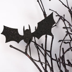 Black glittery halloween bat decoration perched on dark twig-like branches in a halloween bat bouquet