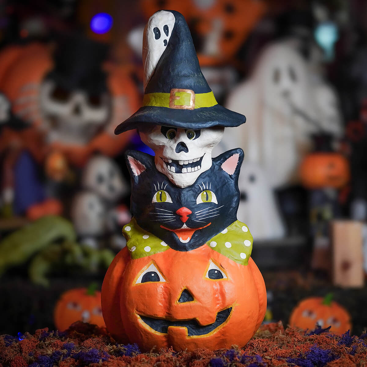 Whimsical halloween totem pole stack with a smiling black cat green polka-dot bow perched on pumpkin topped by ghost in witch hat