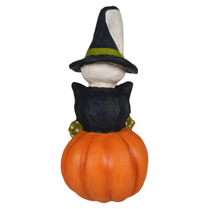 A whimsical halloween totem pole stack with a white witch in a black hat sitting on an orange pumpkin