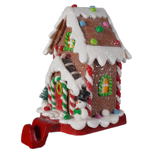 A hand-crafted led lighted gingerbread candy house stocking hanger with glittery brown facade white icing and candy accents