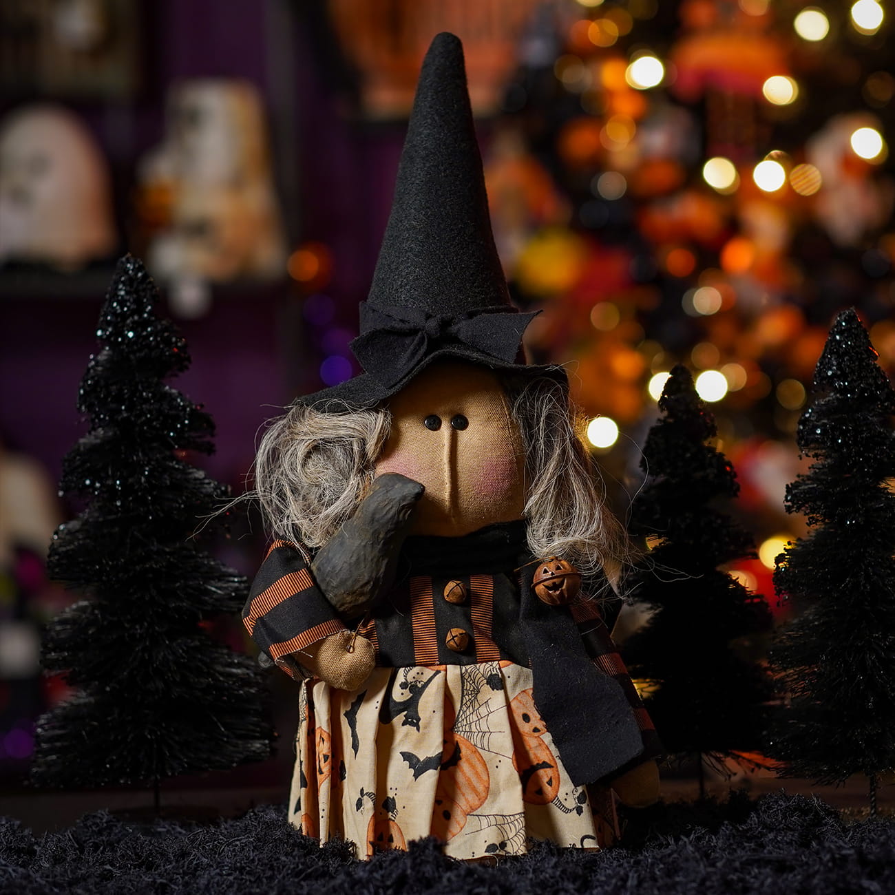 A handcrafted halloween witch doll with gray yarn hair wearing an orange and black figural decor dress holding a crow