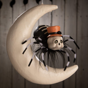 A spooky hanging around spider on moon decoration with a skull spider wearing an orange top hat on a cream crescent moon