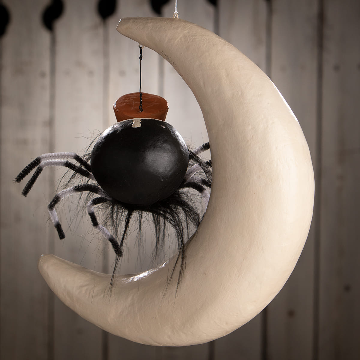 A black spider with fuzzy legs and an orange hat perched on a cream crescent moon decoration spider on moon