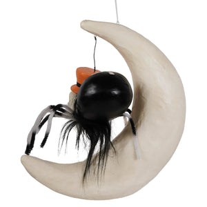 Black spider with orange hat sitting on a cream-colored crescent moon ornament in spider on moon design