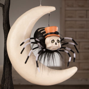 A whimsical hanging around spider on moon decoration with a skull spider, pipe cleaner legs, orange top hat, and crescent moon
