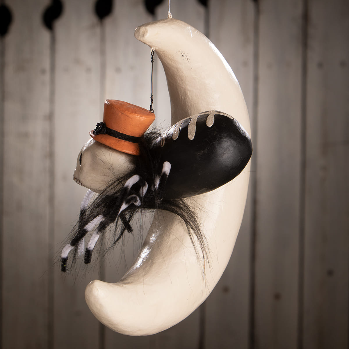A whimsical hanging around spider on moon decoration with a white crescent moon skull orange top hat and faux fur legs