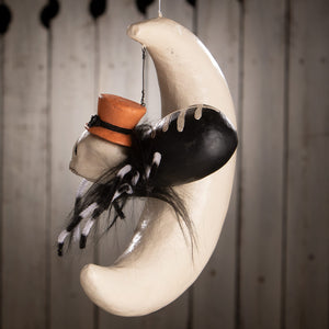 A whimsical hanging around spider on moon decoration with a white crescent moon skull orange top hat and faux fur legs