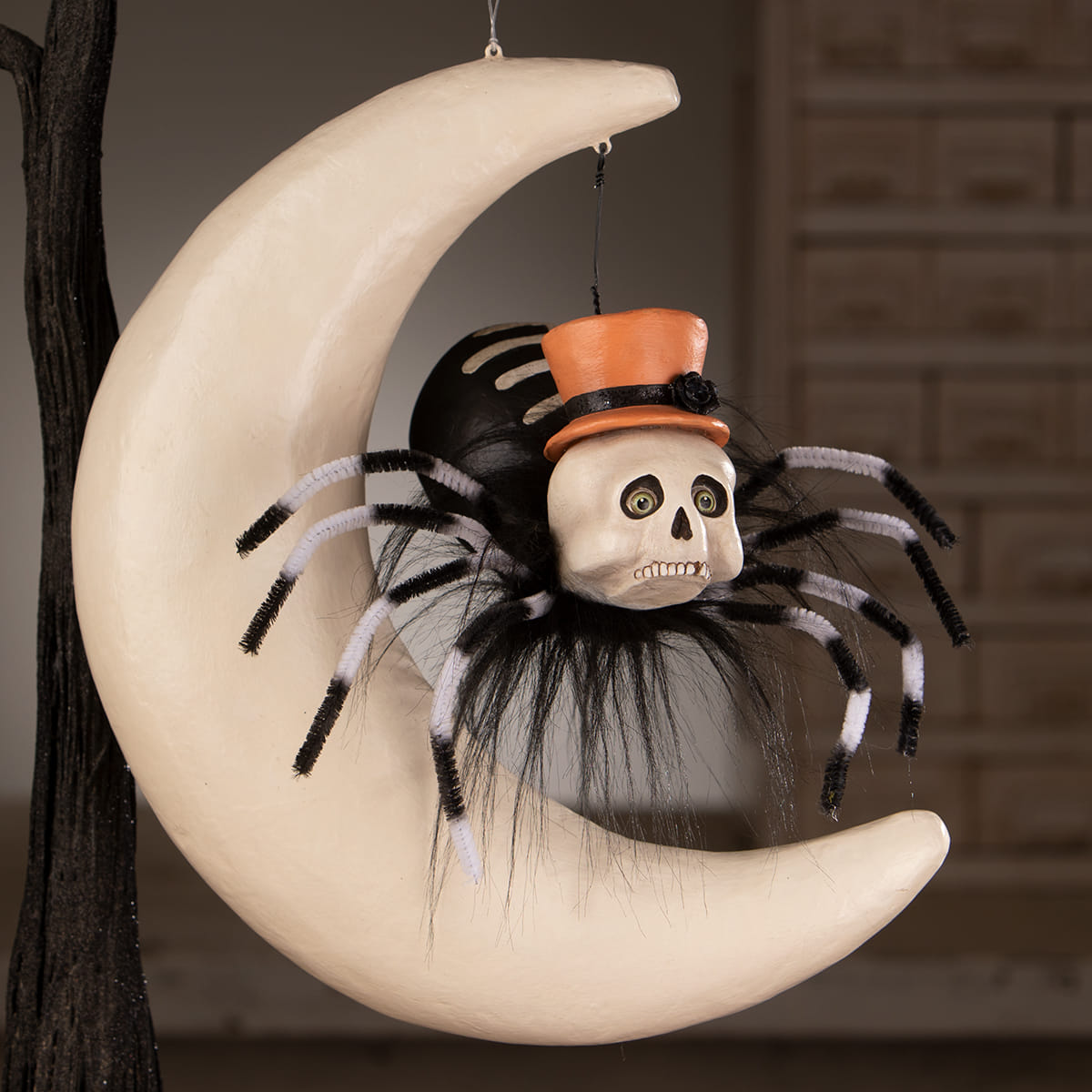 Halloween hanging ornament featuring a black and white pipe cleaner spider on moon with orange top hat on a cream crescent
