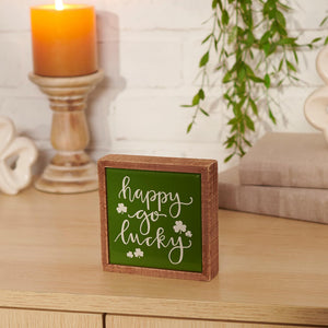 Wooden box sign with ’happy go lucky’ text and shamrocks in green lettering.