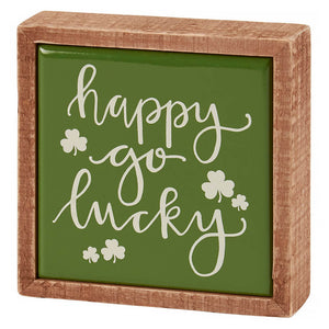 Wooden-framed green sign with ’happy go lucky’ text and shamrock decorations.