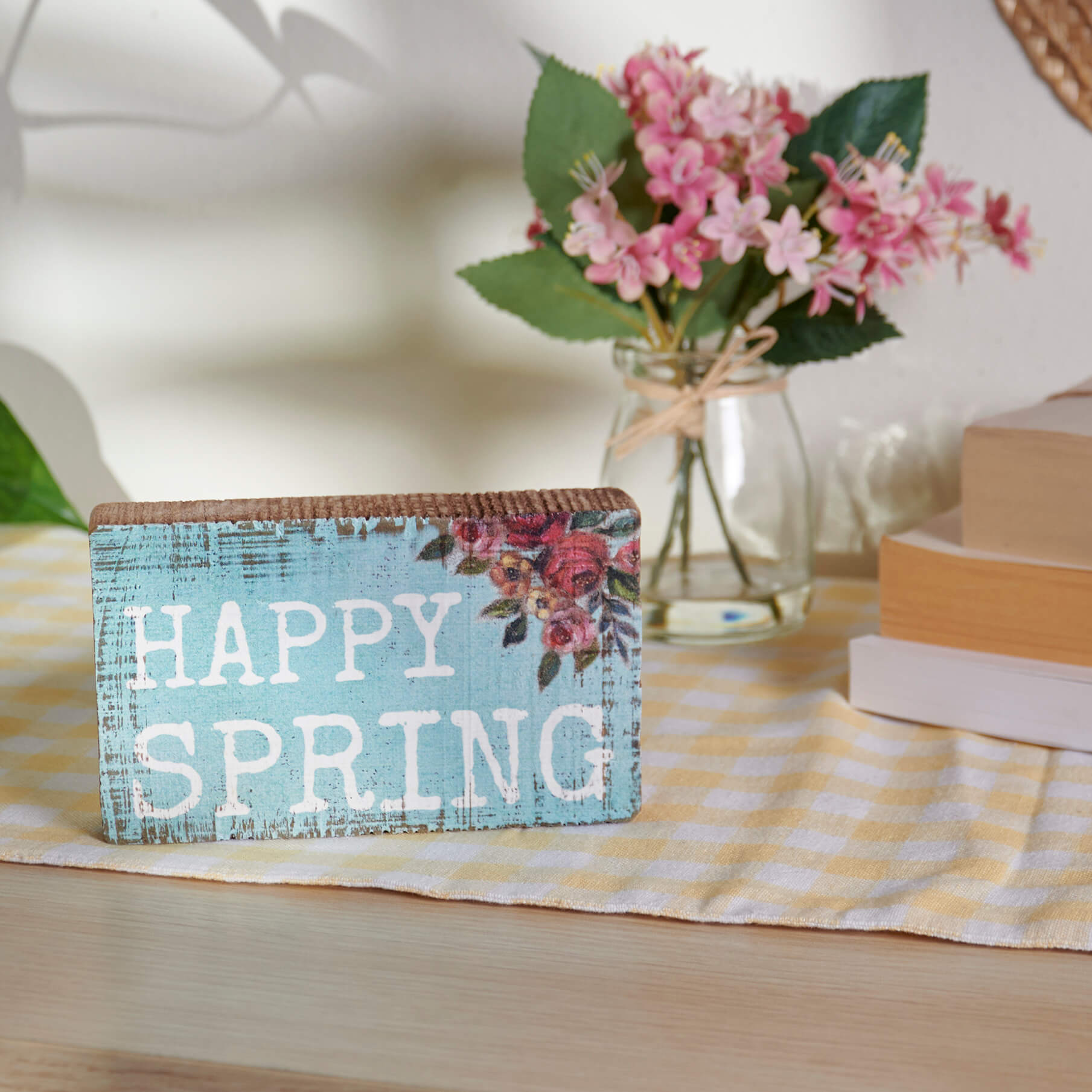 A blue wooden sign with ’Happy Spring’ text and floral accents.