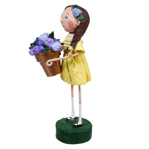 Decorative figurine of a girl in a yellow dress holding purple flowers.