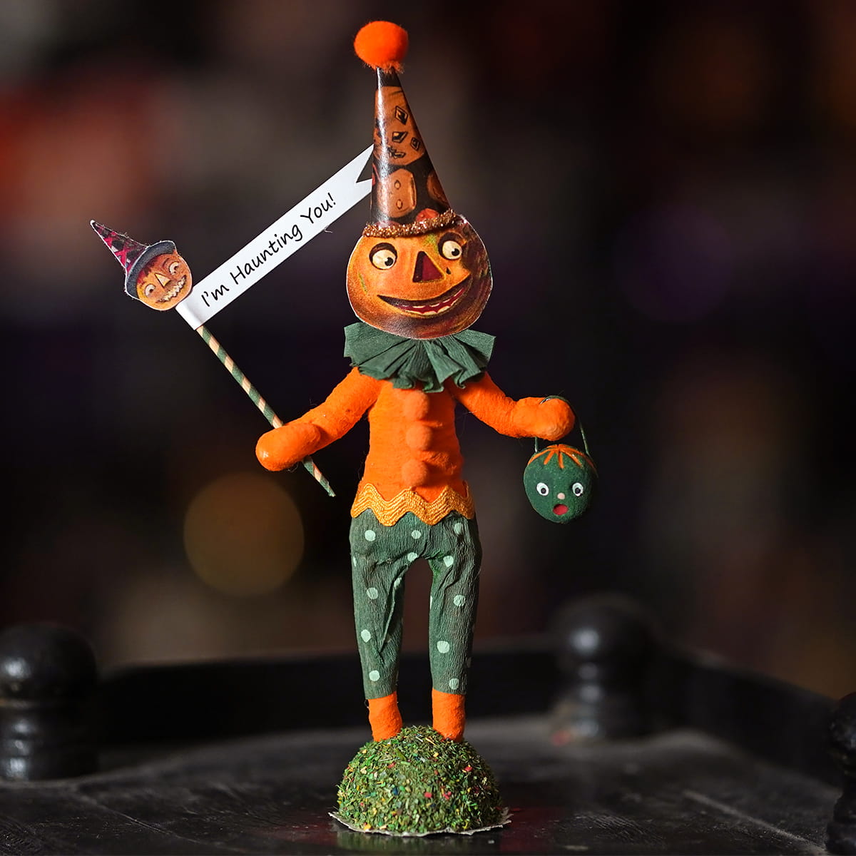 Orange pumpkin-faced halloween scarecrow figurine wearing a patterned party hat holding a sign saying im haunting you haunting pumpkin figure