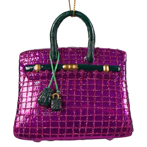 Haute handbag glass ornament featuring a glittery purple luxury handbag with dark green handles and gold-tone hardware