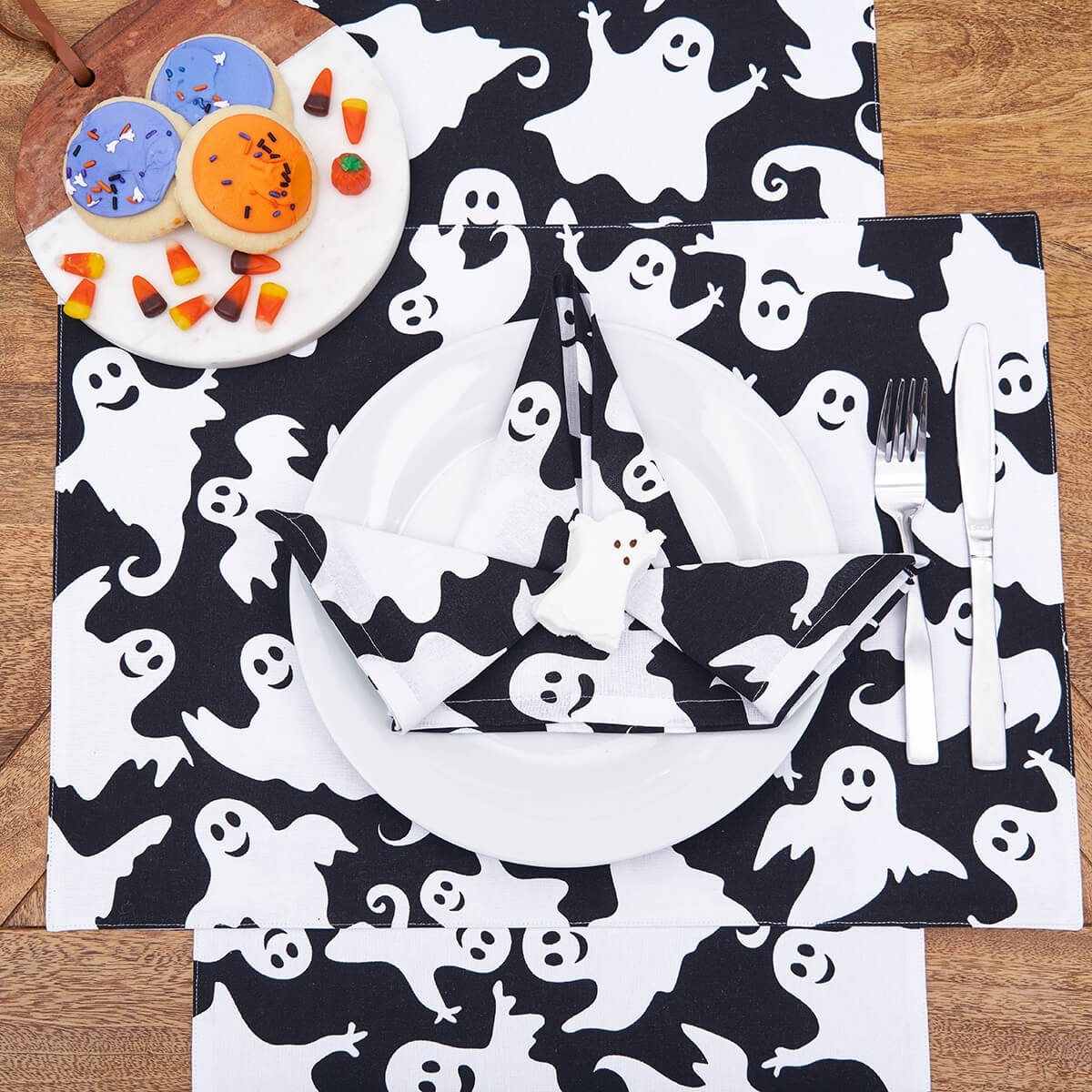 Halloween-themed tablecloth or fabric with a repeating pattern of white cartoon ghosts on a black background.