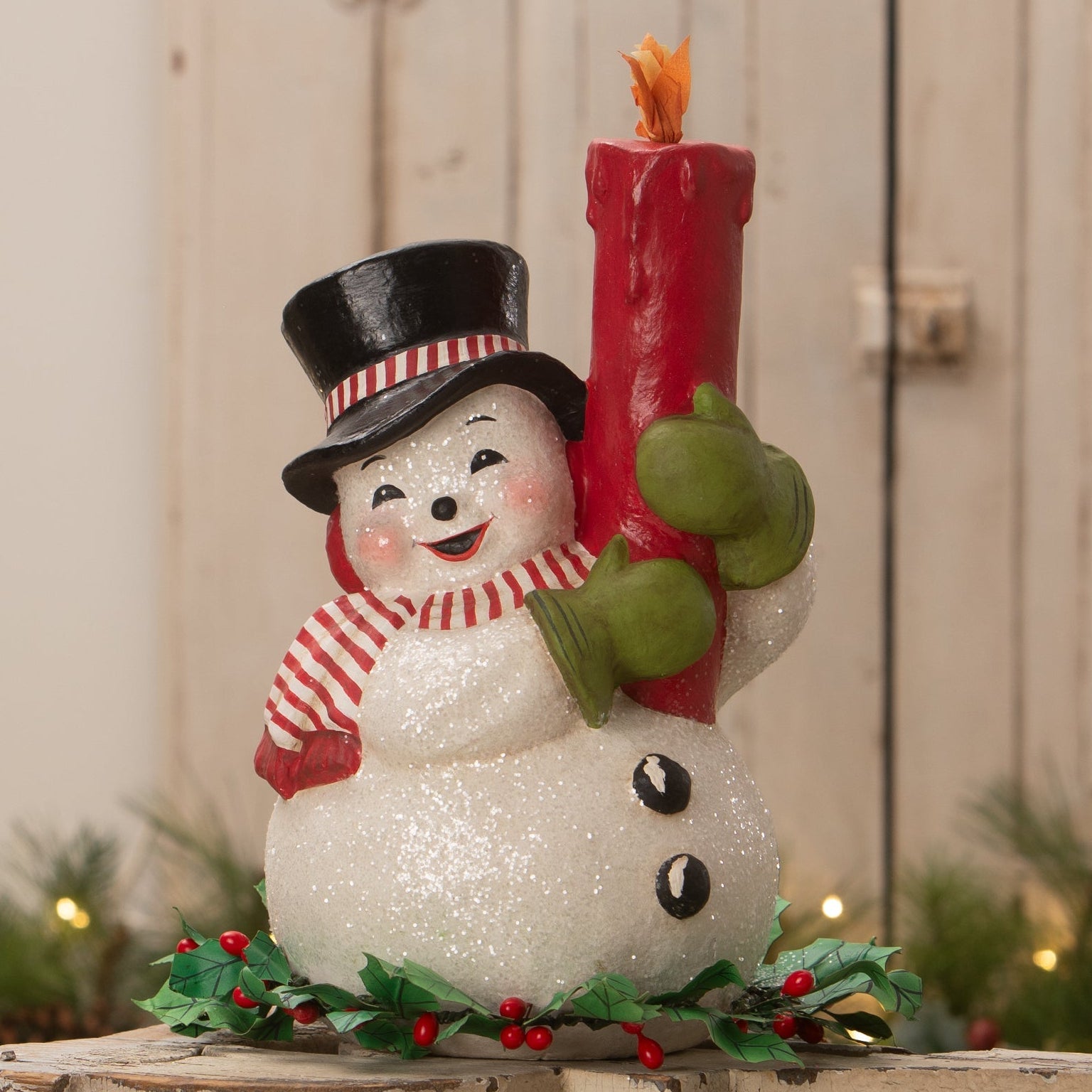 A cheerful white glittery holly berry snowman figurine by bethany lowe designs holding a red candle flame