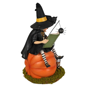 Black witch figurine by bethany lowe designs sitting on an orange pumpkin reading a book with a spider and black cat theme
