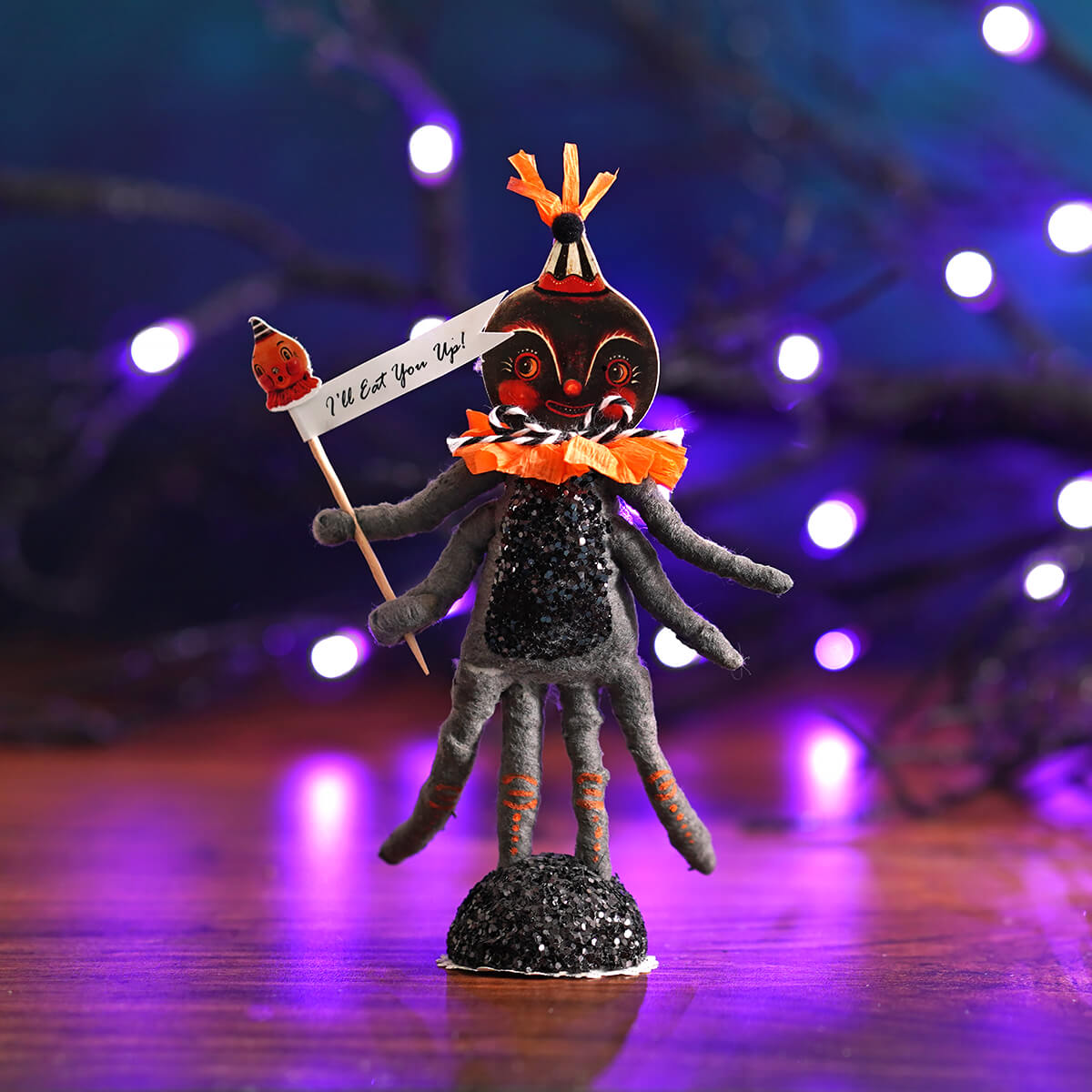 Black glittery halloween spider figure with orange accents and festive hat holding a sign saying ill eat you up