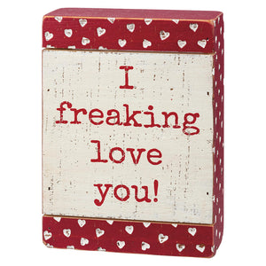 A red and white decorative box sign with the text ’I freaking love you!’ and heart patterns.