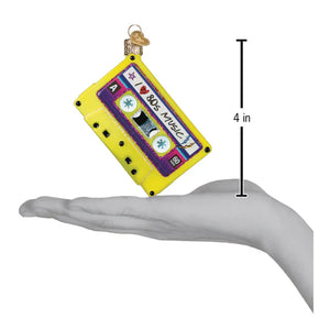 A vibrant yellow and purple christmas glass ornament shaped like a vintage cassette tape with i love 80s music label