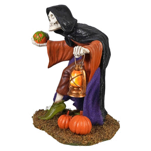 Igor skeleton figure in black cloak and orange robe holding carved pumpkin and lantern on mossy base with pumpkins