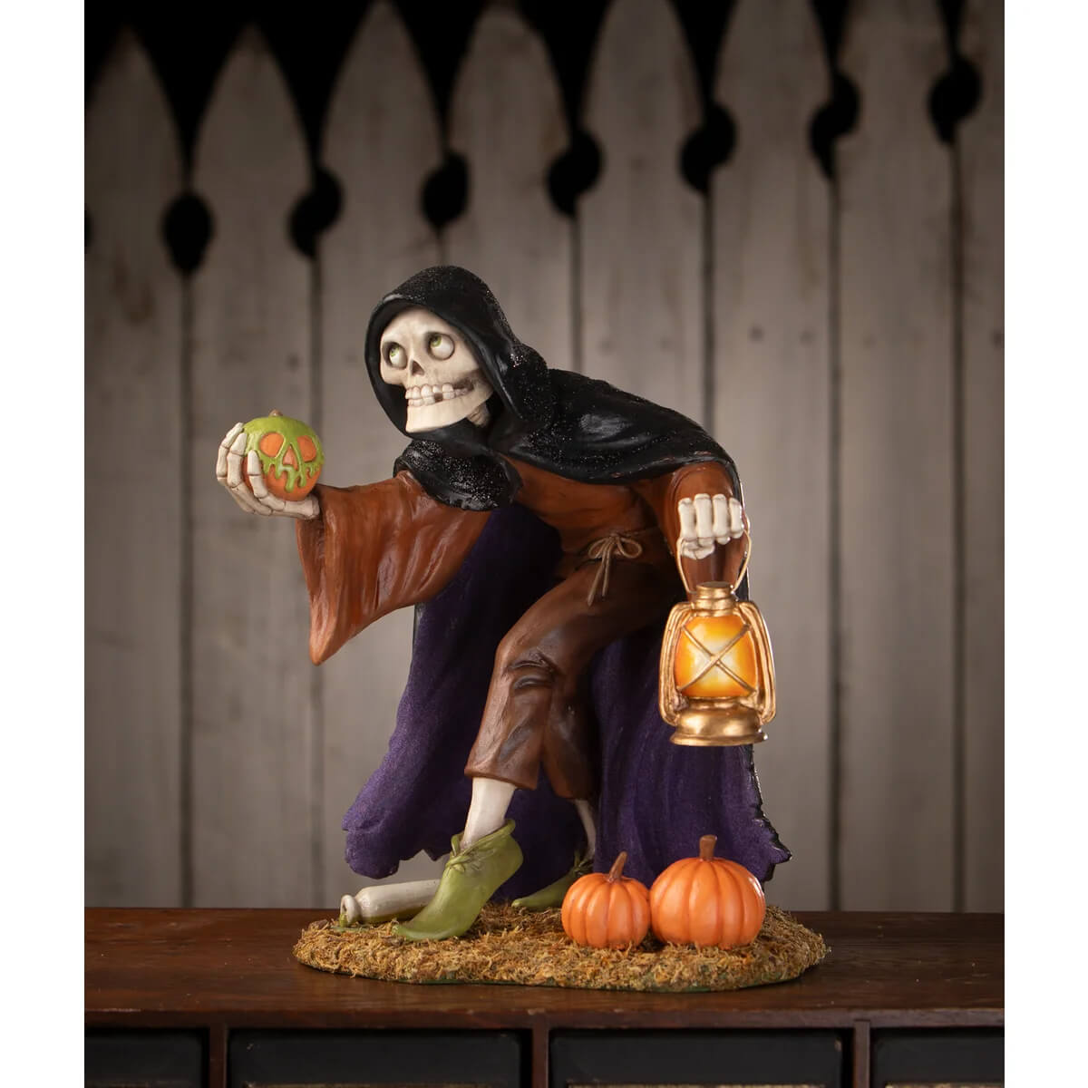 Halloween-themed igor skeleton figure in a black hooded robe holding an orange lantern and carved green pumpkin