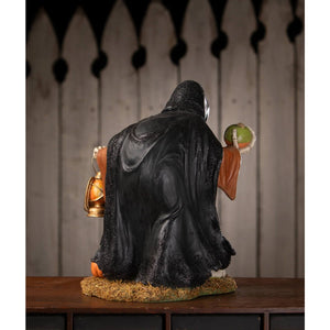 Black textured robe-clad igor skeleton figure with orange accents holding a lantern in one hand