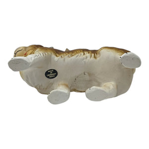 A detailed ceramic figurine of a sleeping dog with white and tan fur next to an ino schaller walking easter bunny paper mache