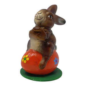 Brown ceramic rabbit figurine sitting on a red orange egg with flowers on a green base ino schaller easter german paper