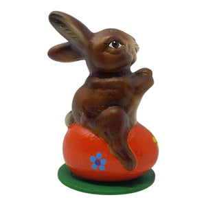 Brown ceramic schaller easter bunny sitting on orange egg with blue flowers on green base german paper mache decor