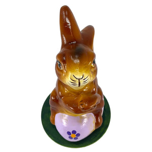 A glossy brown ceramic ino schaller easter bunny with black whiskers sitting on a purple german paper mache egg