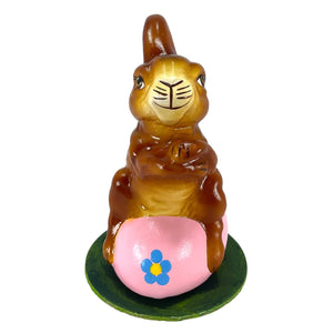 A glossy brown ino schaller easter rabbit figurine with black whiskers on a pink hand-painted paper mache egg