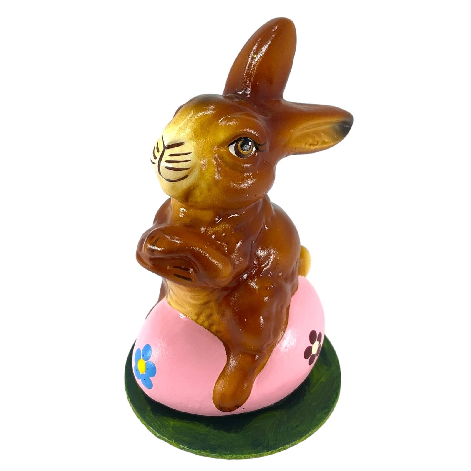 A glossy brown ino schaller easter paper mache bunny sits on a pink egg with blue and purple flowers