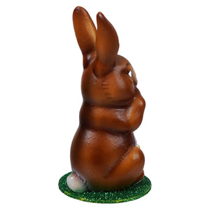 Ino schaller sitting brown chocolate bunny holding yellow basket on a glittery green base for easter decor