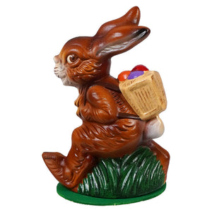 Ino schaller walking brown chocolate easter bunny carrying a basket of colorful eggs on a green grassy base