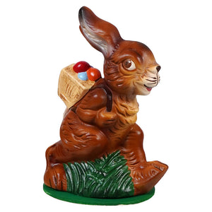 Ino schaller walking brown ceramic easter bunny carrying a basket of colorful eggs on green grass base