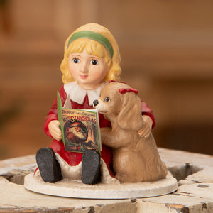 A porcelain bethany lowe figurine of a blonde girl in red reading the night before christmas to a tan puppy with a red bow