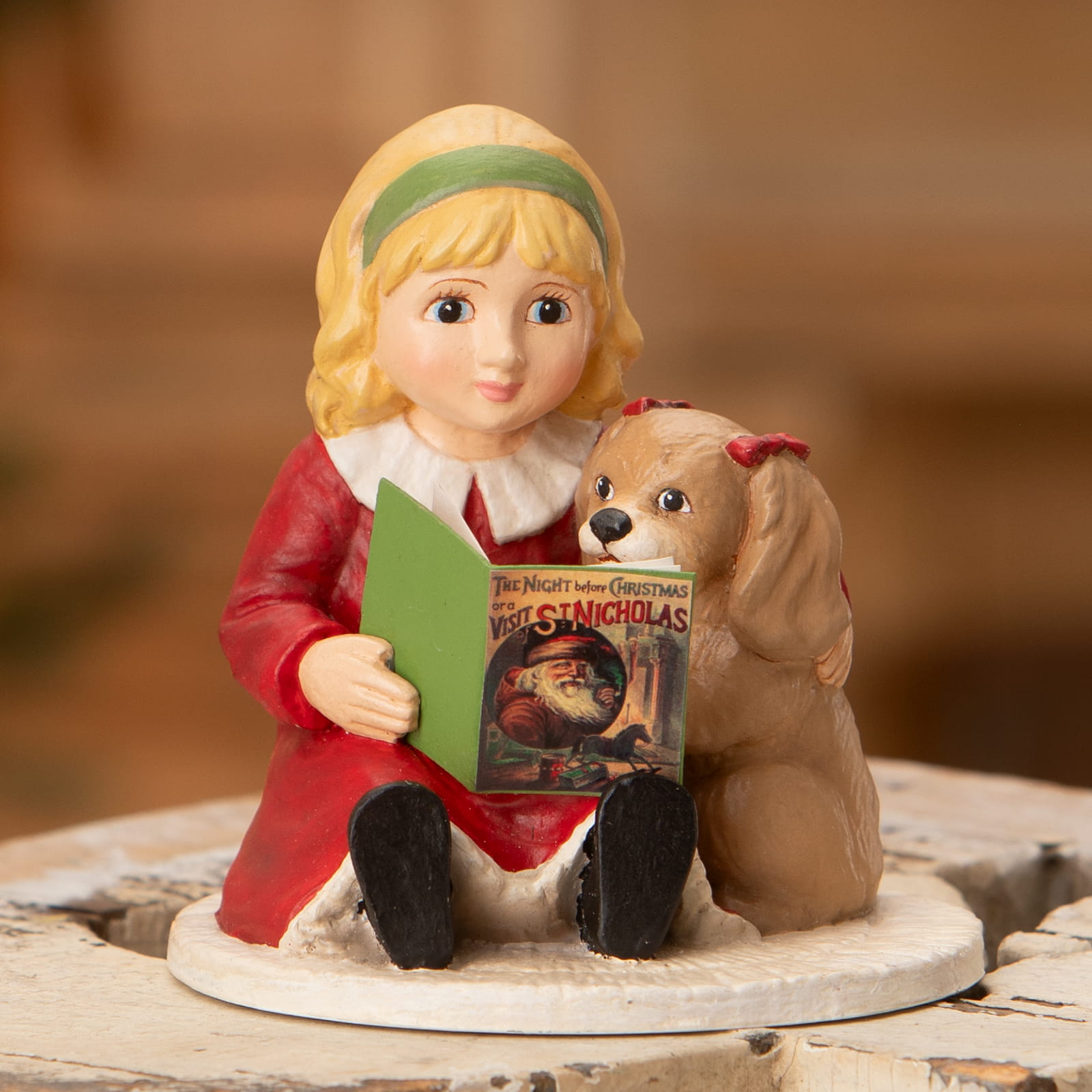 A bethany lowe porcelain figurine of isla reading to a puppy with a red bow and an open book about christmas