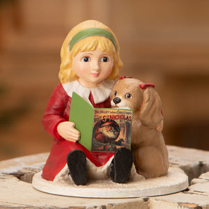 A bethany lowe porcelain figurine of isla reading to a puppy with a red bow and an open book about christmas