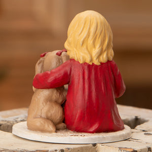 A resin bethany lowe figurine of a blonde girl in a red coat hugging a tan puppy with red bows on its ears