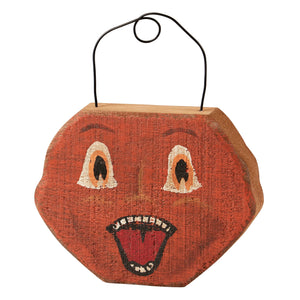 A rustic orange wooden jack face chunky hanging ornament with painted cartoonish eyes and a wide open mouth